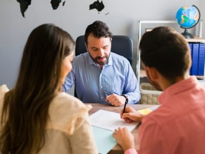 You got a deal. Young man signing a sales contract for a holiday vacation with his wife. Sales representative closing a deal for a timeshare sale with some customers at the travel agency
